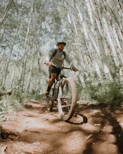 Mountain biker riding on a narrow trail with towering trees on both sides.