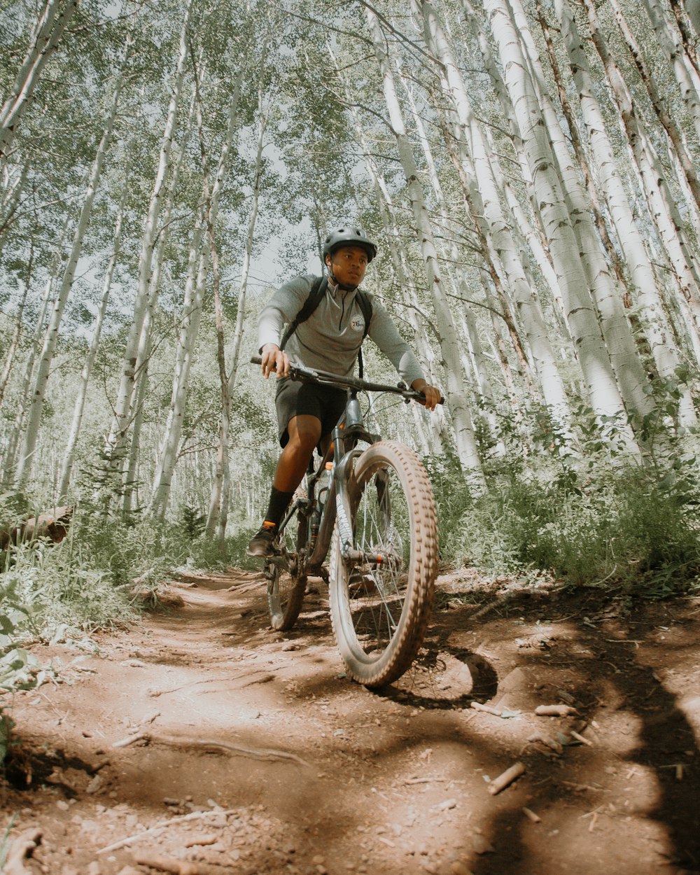 woman in gray jacket riding bicycle on forest during daytime