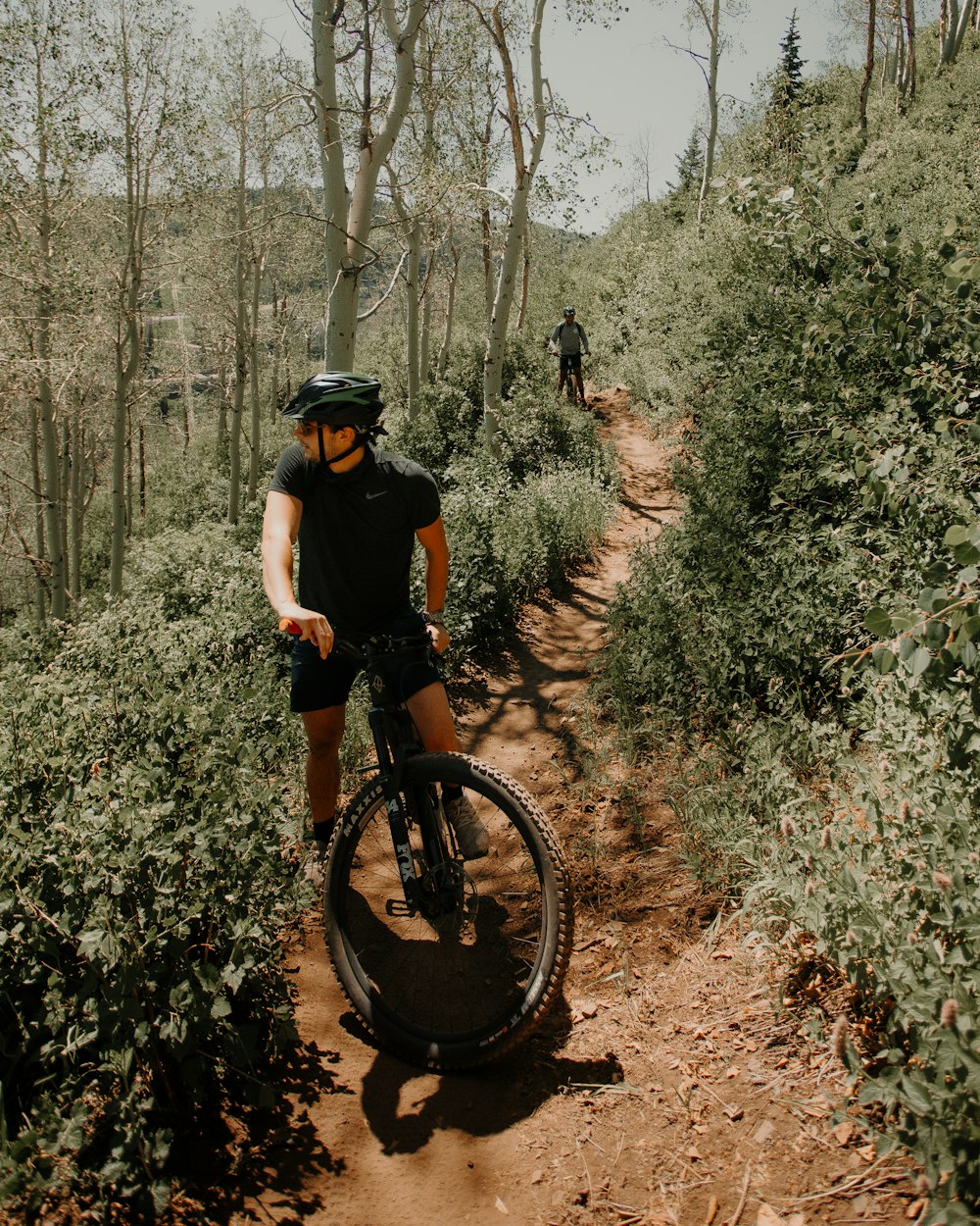 man in black t-shirt riding bicycle on forest during daytime