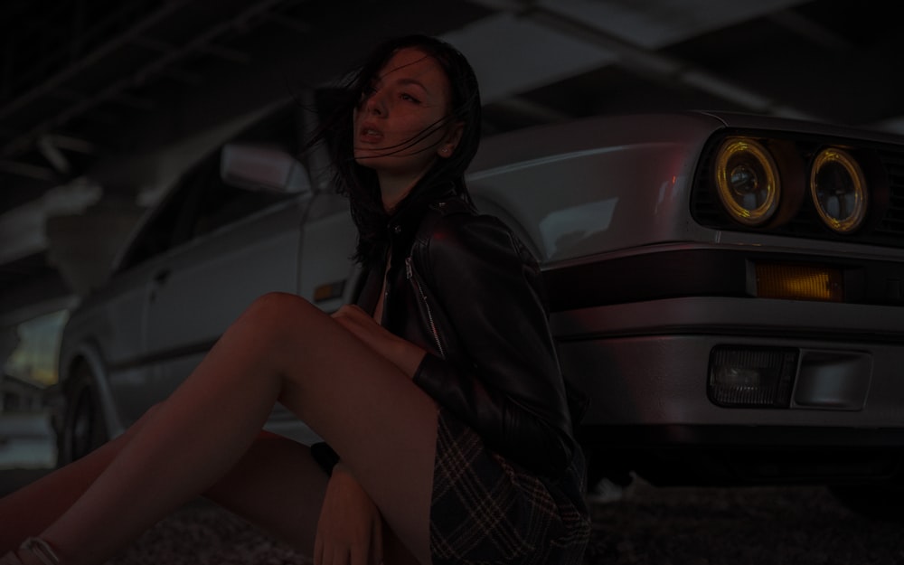 woman in black leather jacket sitting on gray concrete floor