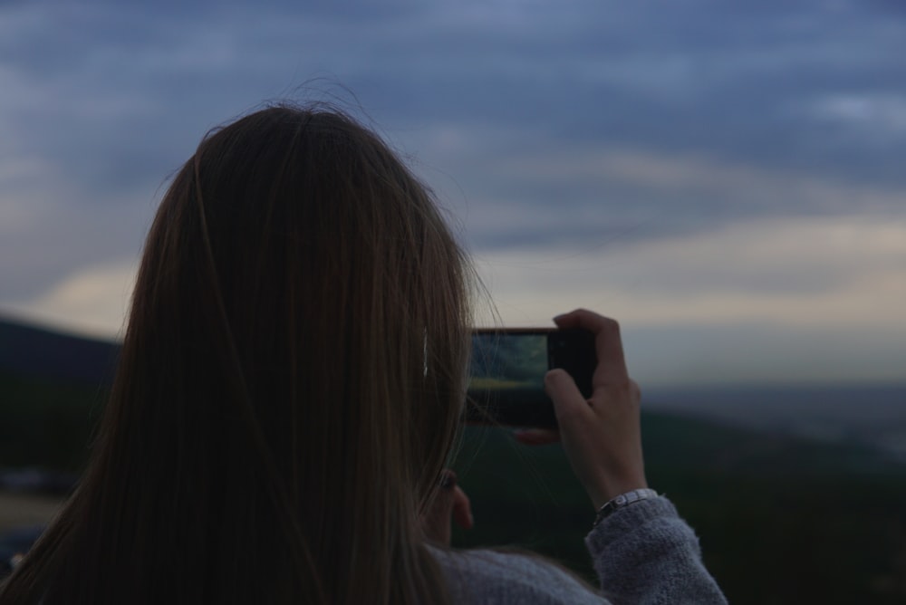 woman in gray sweater taking photo of clouds