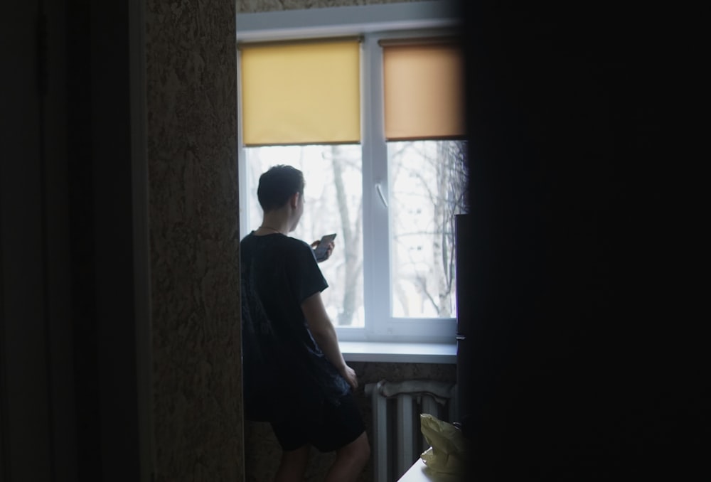 man in black t-shirt standing near window