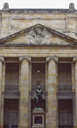 woman in green jacket standing in front of beige concrete building
