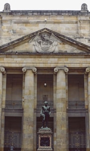 woman in green jacket standing in front of beige concrete building