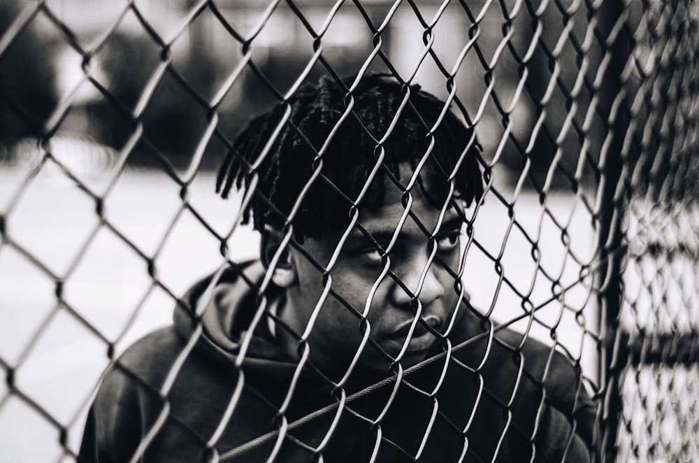 man in black jacket leaning on chain link fence