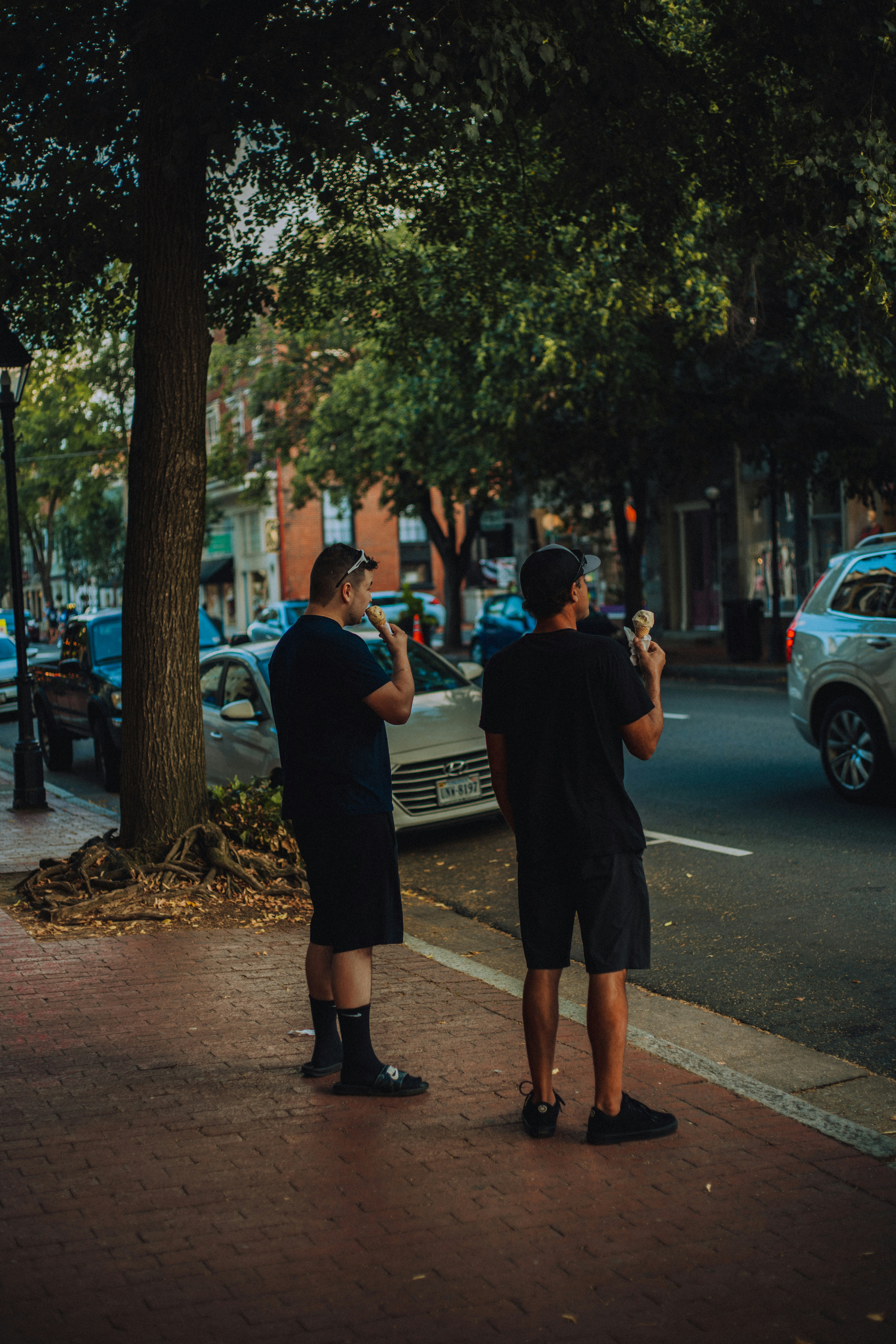 man in black t-shirt and black shorts standing on sidewalk during daytime