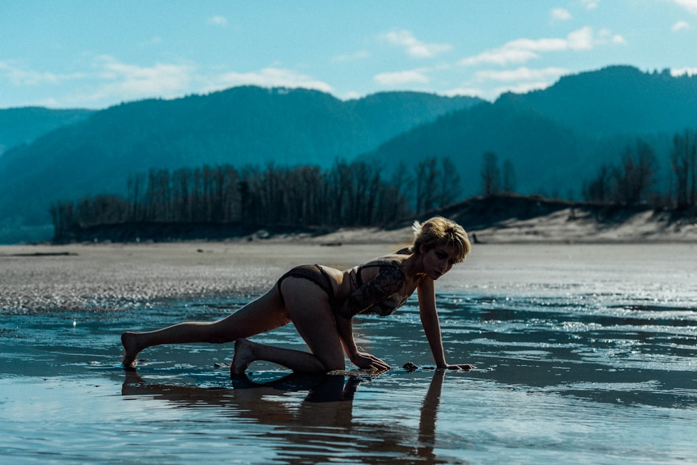 woman in black tank top and black shorts sitting on brown wooden log on body of near on near on