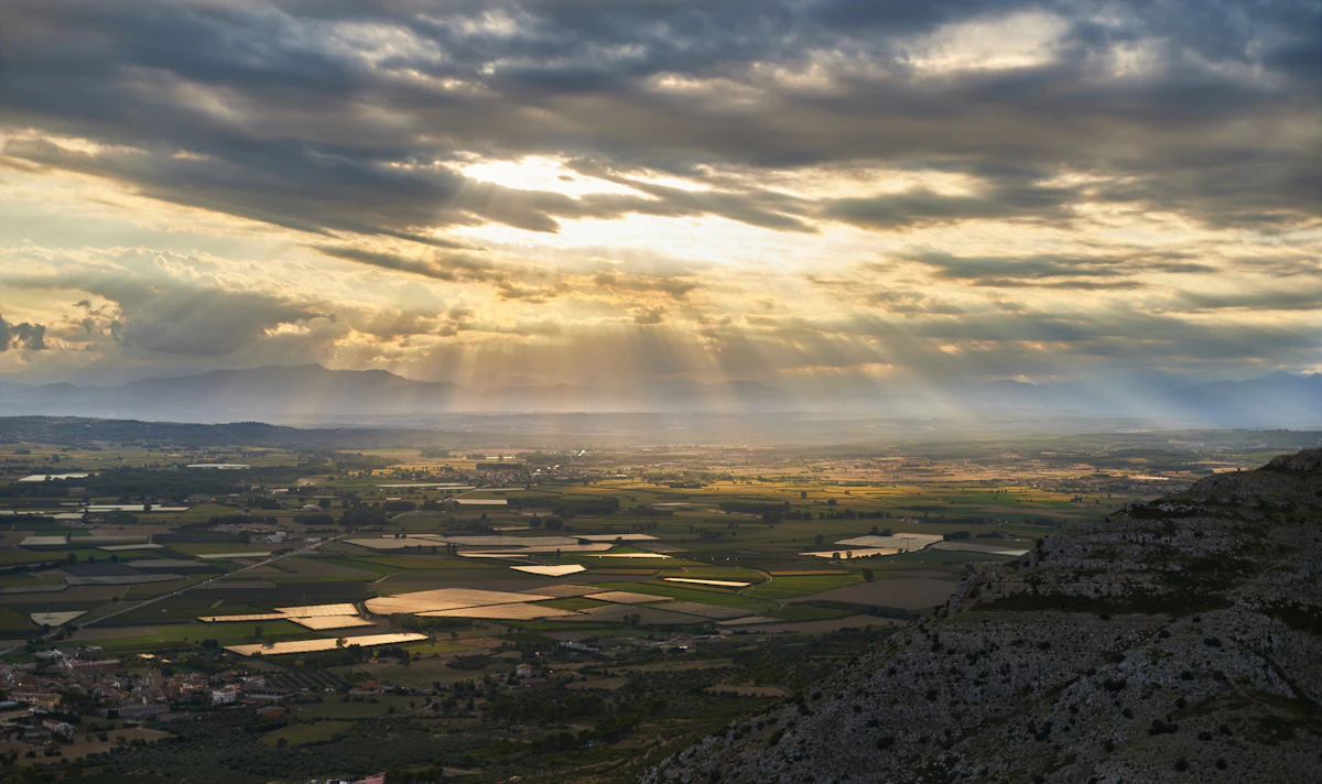 Sun breaking through clouds over the flat fields around Torroella de Montgrí, seen from a rocky hillside