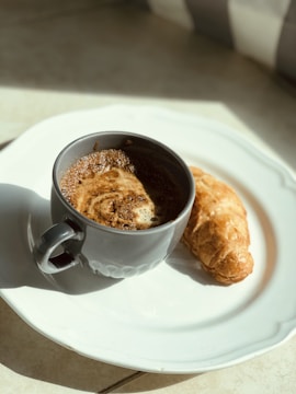 A warm coffee cup beside a plate of delicate pastries on a sunlit café table.