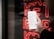A hand holding a smartphone displaying a list of recent calls, mostly marked as spam or telemarketing. In the background, there is a neon red sign with indistinct letters or symbols.