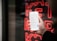 A hand holding a smartphone displaying a list of recent calls, mostly marked as spam or telemarketing. In the background, there is a neon red sign with indistinct letters or symbols.