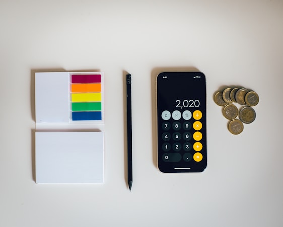 A phone calculator and a small stack of coins on a desk