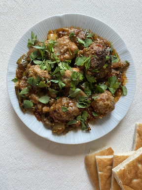 Close-up photo of a wooden plate with a variety of bite-sized meatballs and fresh herbs.
