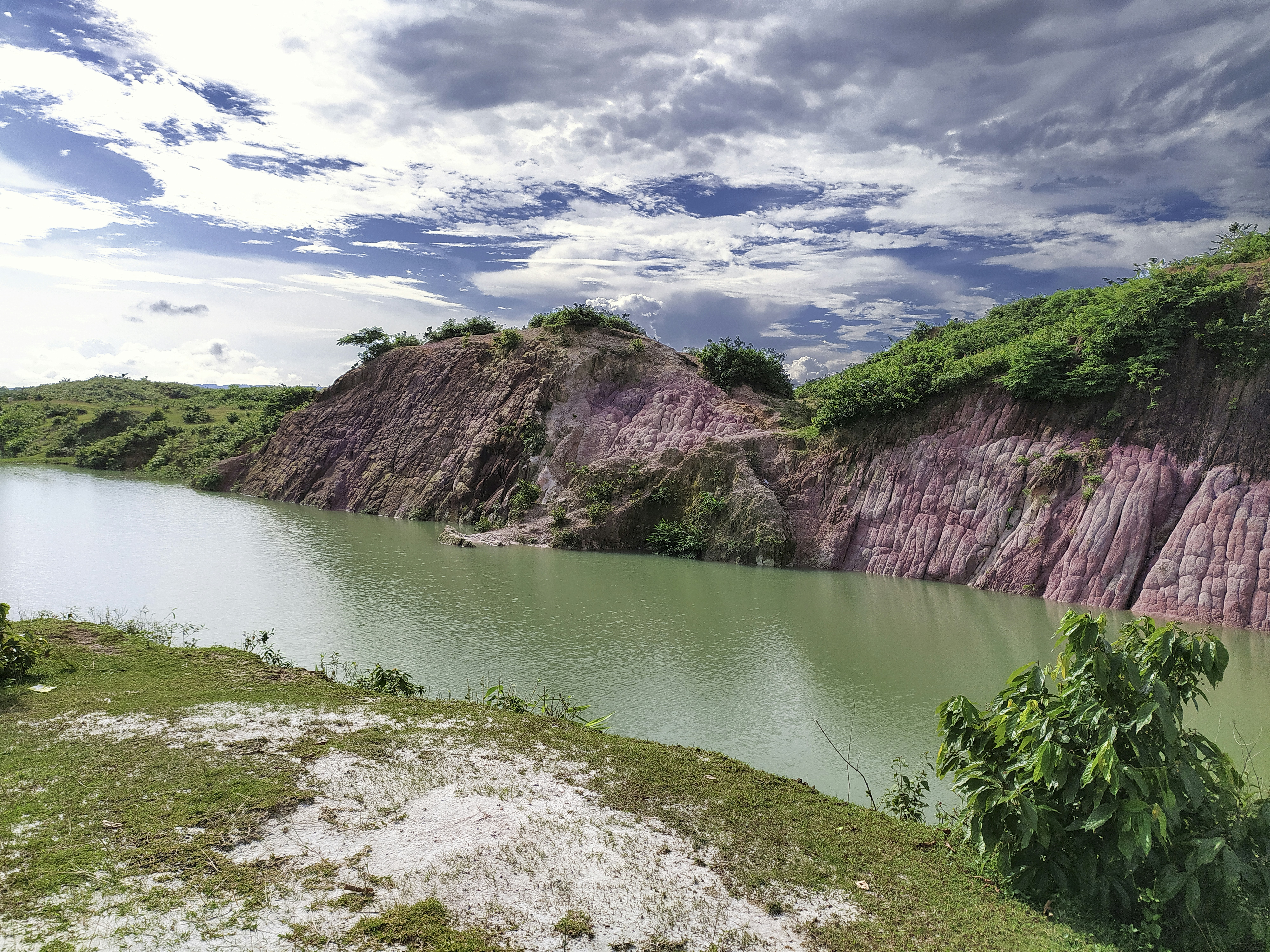 green lake between brown mountains under white clouds and blue sky during daytime
