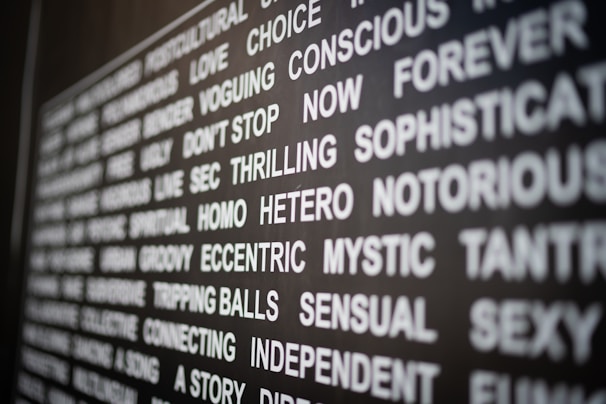 A close-up of a wall or board covered with various words in bold white letters, each conveying different emotions or concepts, on a dark background. The perspective is slightly angled, adding depth.
