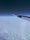 An airplane wing extends over a blanket of fluffy white clouds, with a gradient sky transitioning from dark blue at the top to lighter hues near the horizon.