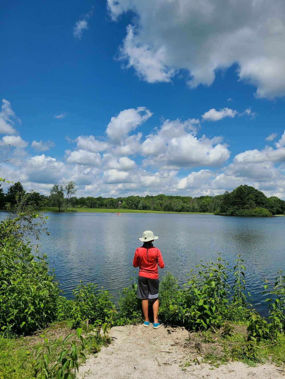 person in red shirt standing near lake during daytime