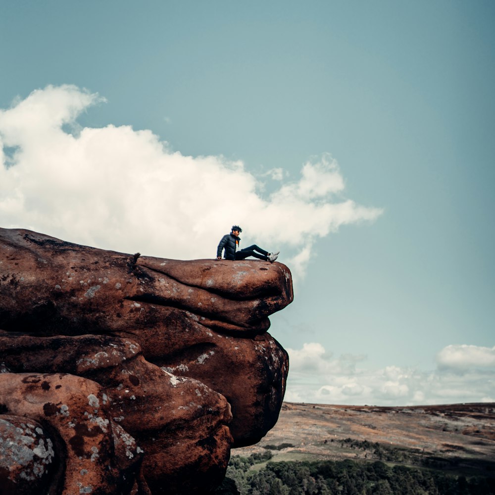 man in black jacket sitting on brown rock formation during daytime