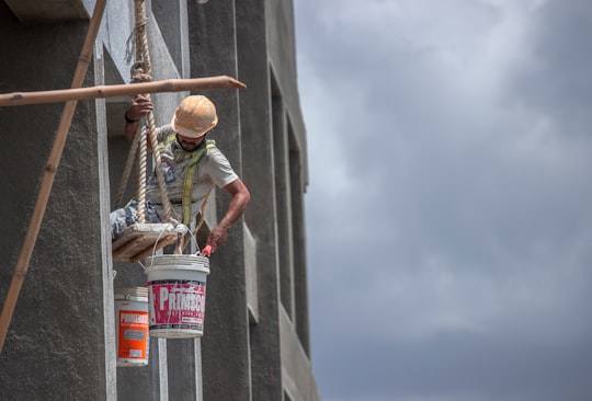 man in green t-shirt and brown hat climbing on gray concrete wall during daytime in Pune India