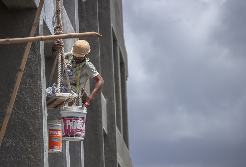 man in green t-shirt and brown hat climbing on gray concrete wall during daytime