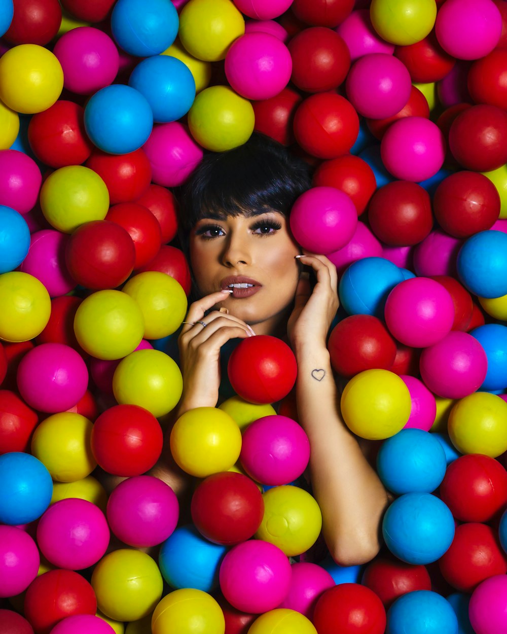 woman in white tank top with assorted color balloons on her face