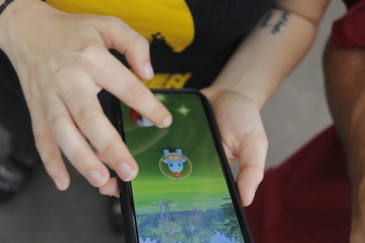 A person is interacting with a smartphone, playing a game that involves a virtual character on the screen. The hand is poised to tap or swipe, indicating engagement with the game.