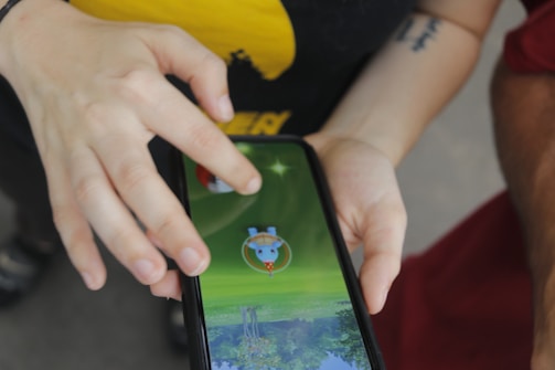 A person is interacting with a smartphone, playing a game that involves a virtual character on the screen. The hand is poised to tap or swipe, indicating engagement with the game.