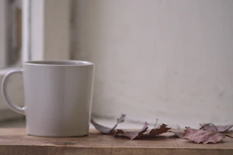 A cozy handmade ceramic mug with a deep carmine glaze resting on a wooden table with autumn leaves.