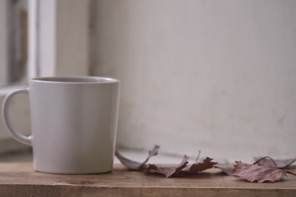 A cozy handmade ceramic mug with a deep carmine glaze resting on a wooden table with autumn leaves.