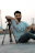 man in teal crew neck t-shirt sitting on black and gray tripod