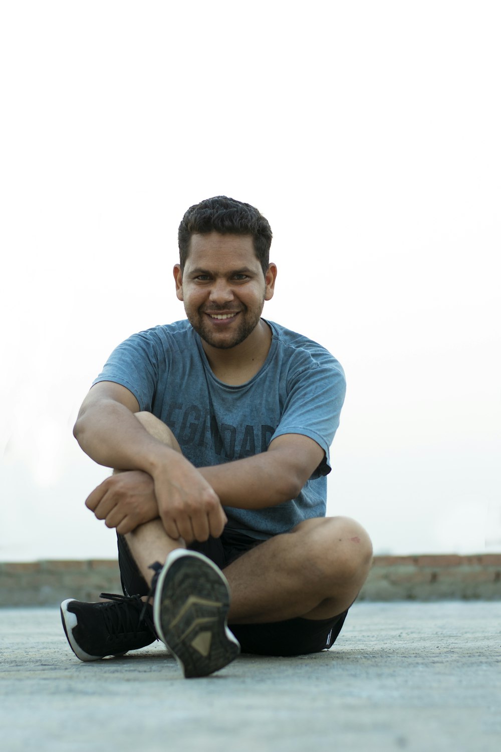 man in blue crew neck t-shirt sitting on brown wooden bench during daytime