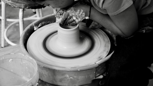 Artist shaping clay on a pottery wheel in a sunlit studio.
