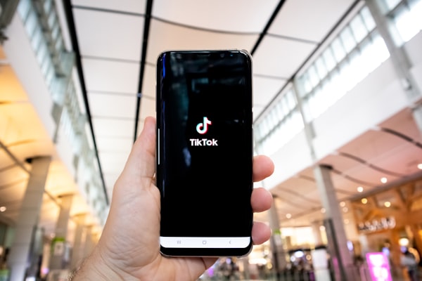 a hand holding up an Android phone with the TikTok launch screen on display, with a shopping mall in the background