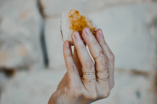 A graceful hand wearing multiple rings with crystals, set against a pale, airy background.