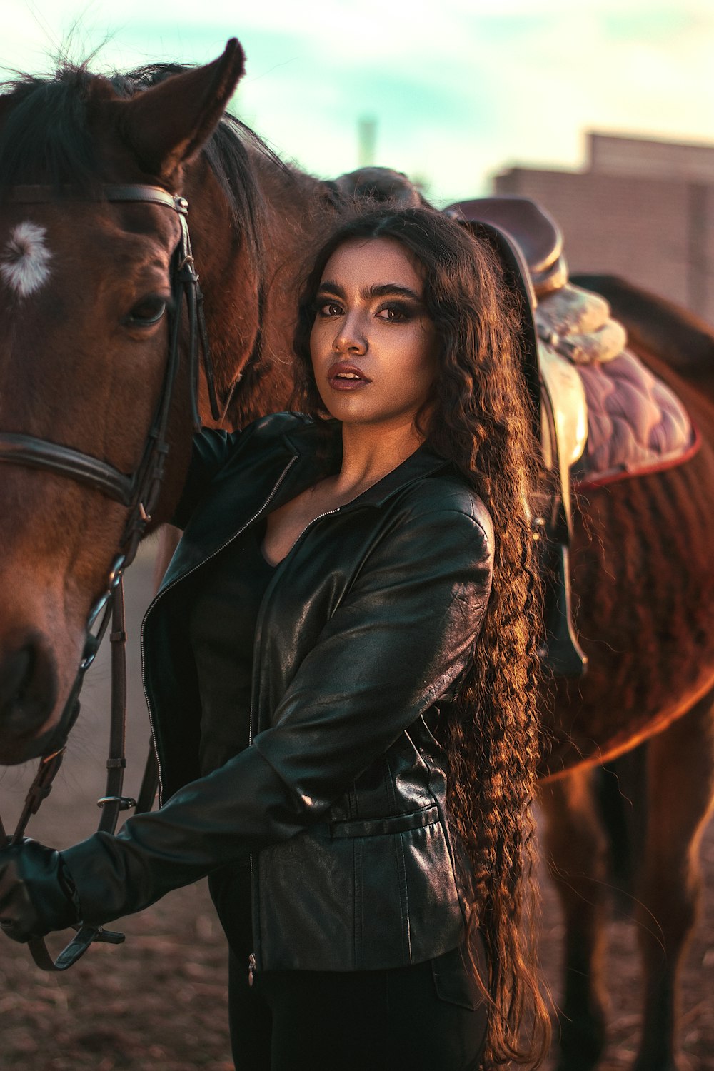 woman in black leather jacket standing beside brown horse