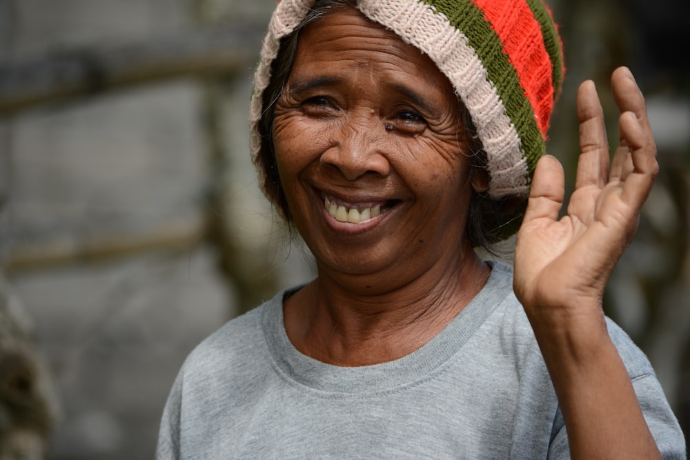 smiling woman in gray crew neck shirt wearing white red and green knit cap