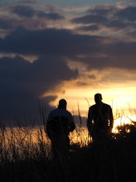silhouette of 2 men standing on grass field during sunset