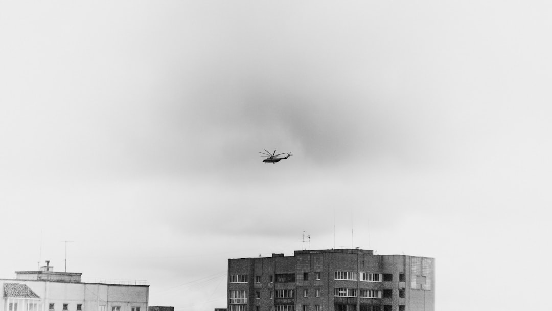 grayscale photo of airplane flying over city buildings