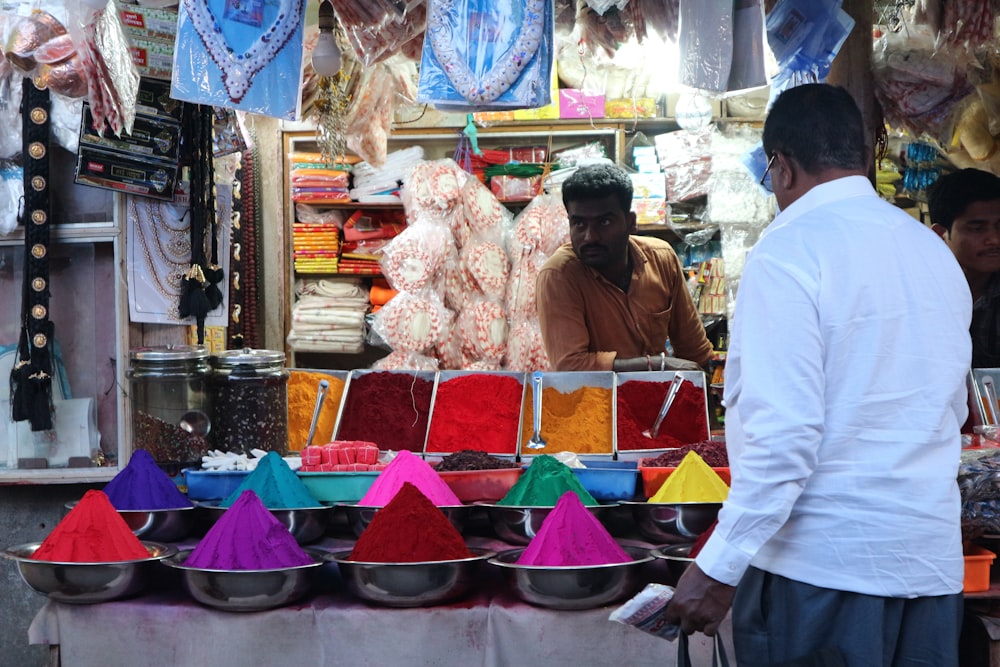 man in white long sleeve shirt standing beside red and green plastic food stall