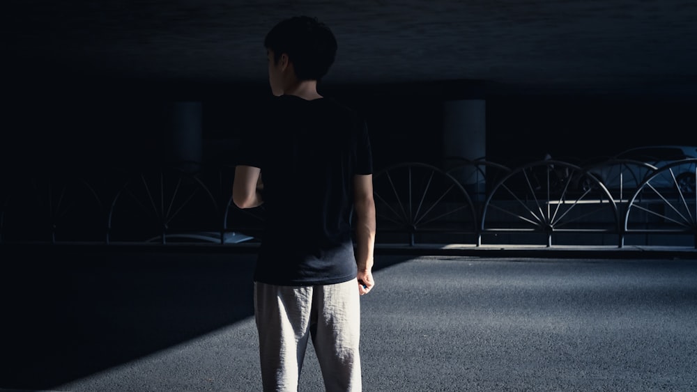 man in black crew neck t-shirt and white pants standing on road during nighttime