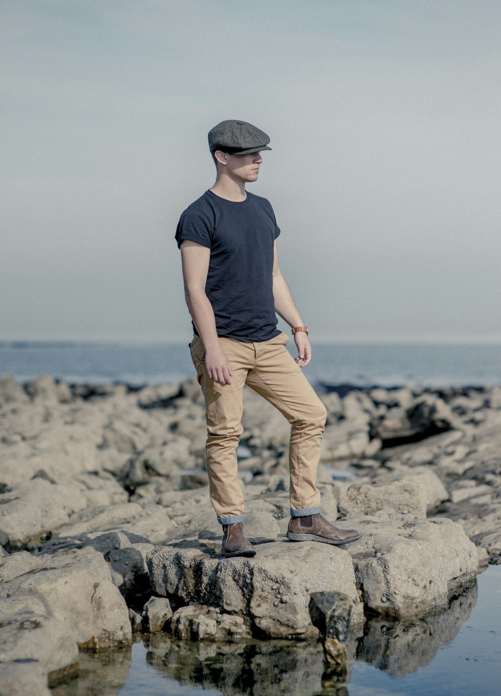 man in black crew neck t-shirt and brown pants standing on gray rock near body