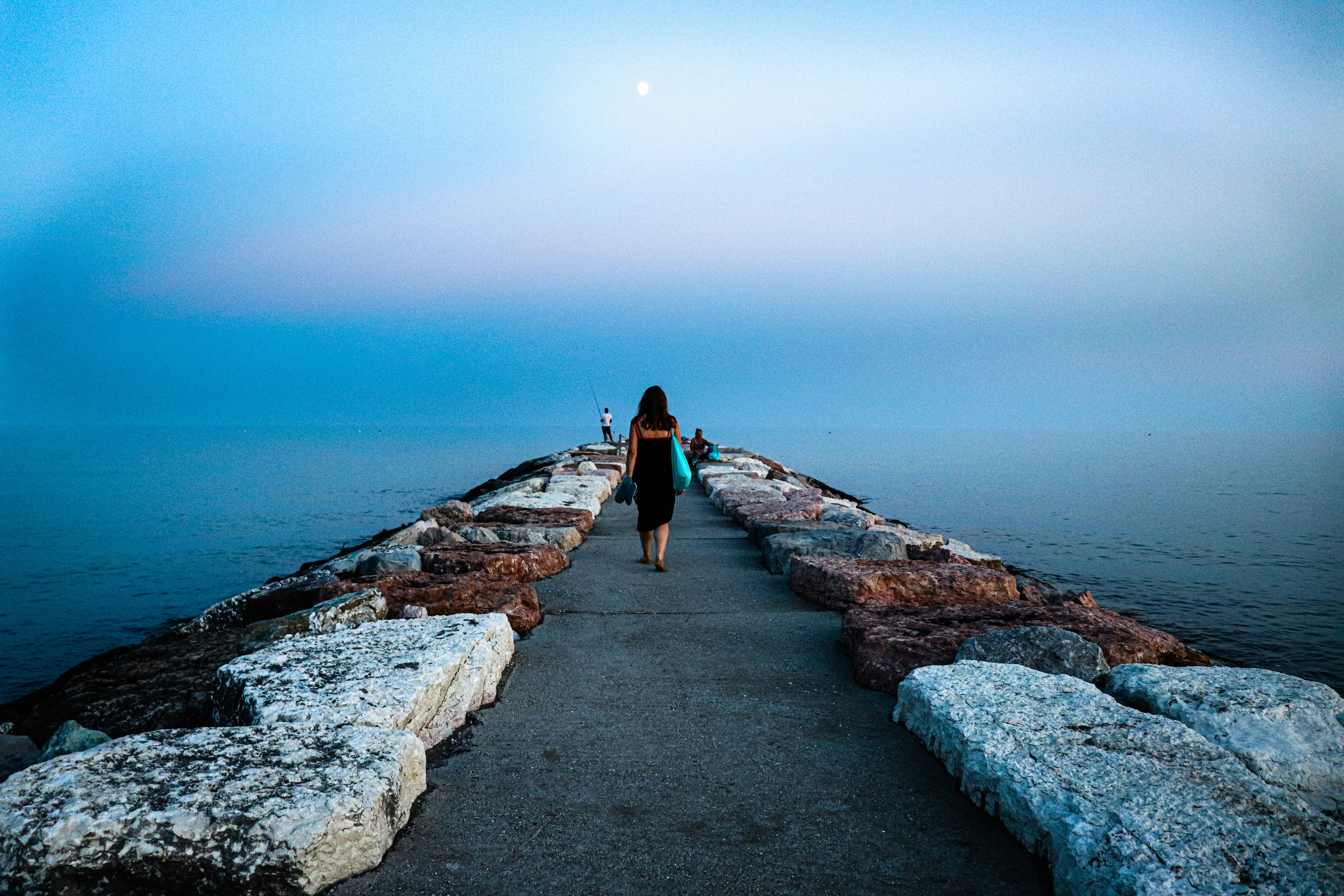 昼間に水域近くの灰色のコンクリートの小道を歩く黒いジャケットを着た女性