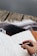A hand holding a black pen is poised to write in an open notebook filled with cursive writing. The notebook rests on a surface covered with a patterned blanket, suggesting a cozy environment. The background features a wooden texture, possibly the edge of a porch or a rustic table.