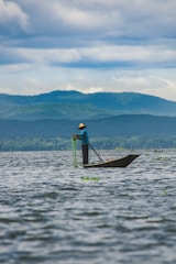 man in blue shirt and brown hat standing on brown wooden boat on sea during daytime