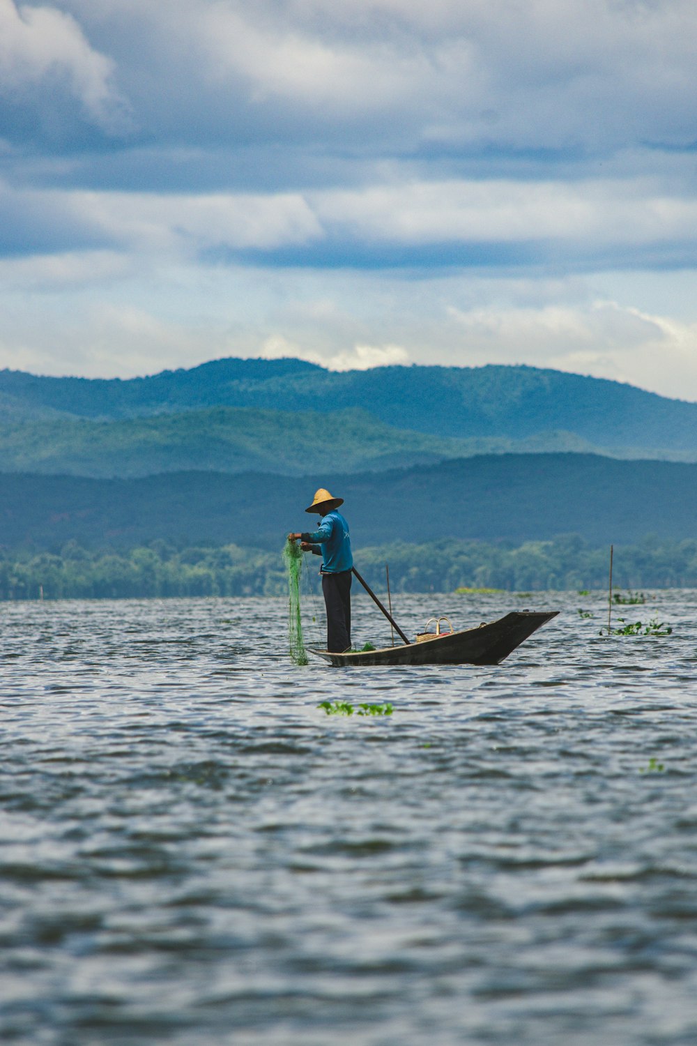 man in blue shirt and brown hat standing on brown wooden boat on sea during daytime