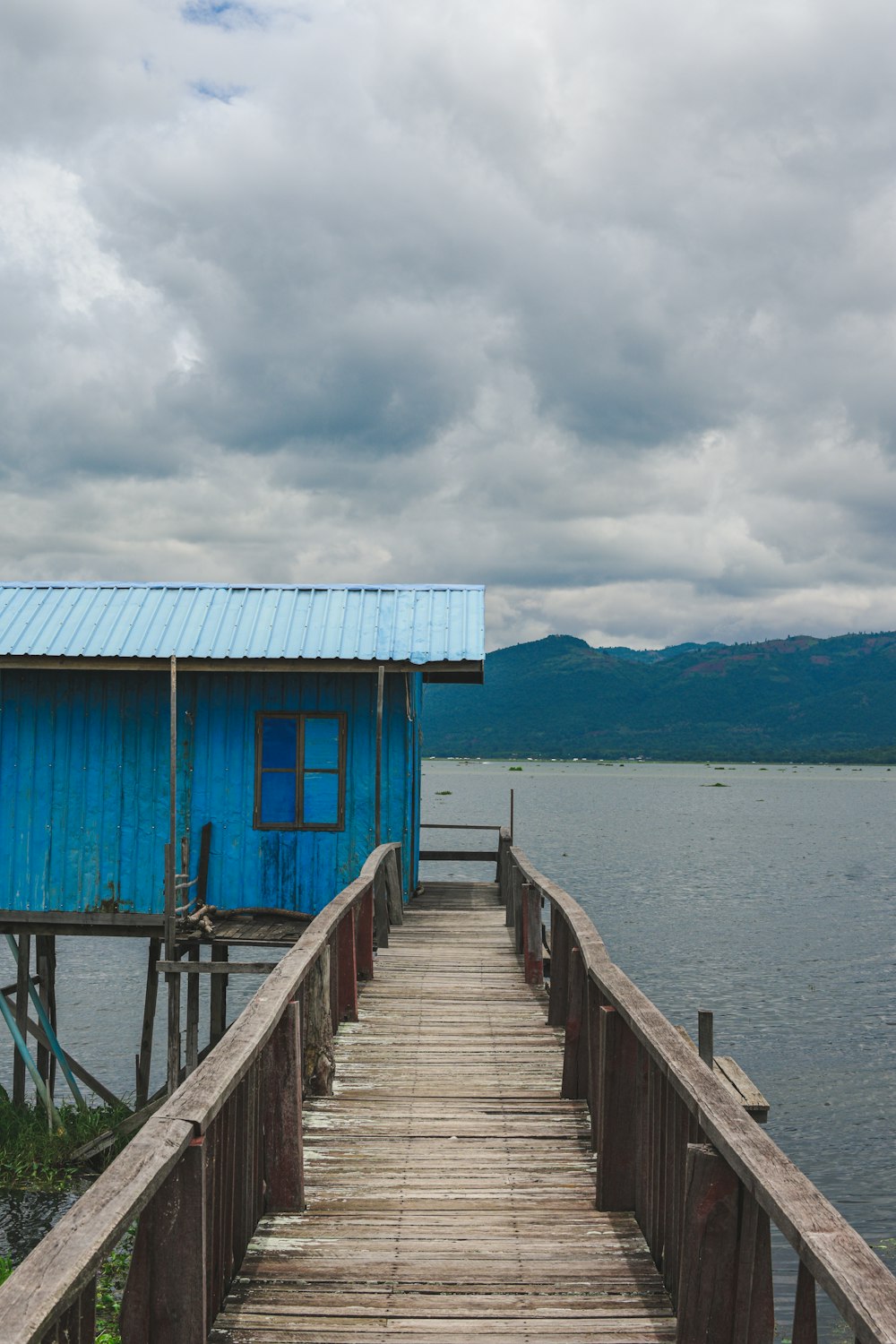 casa de madeira azul na doca perto do corpo de água sob o céu nublado durante o dia