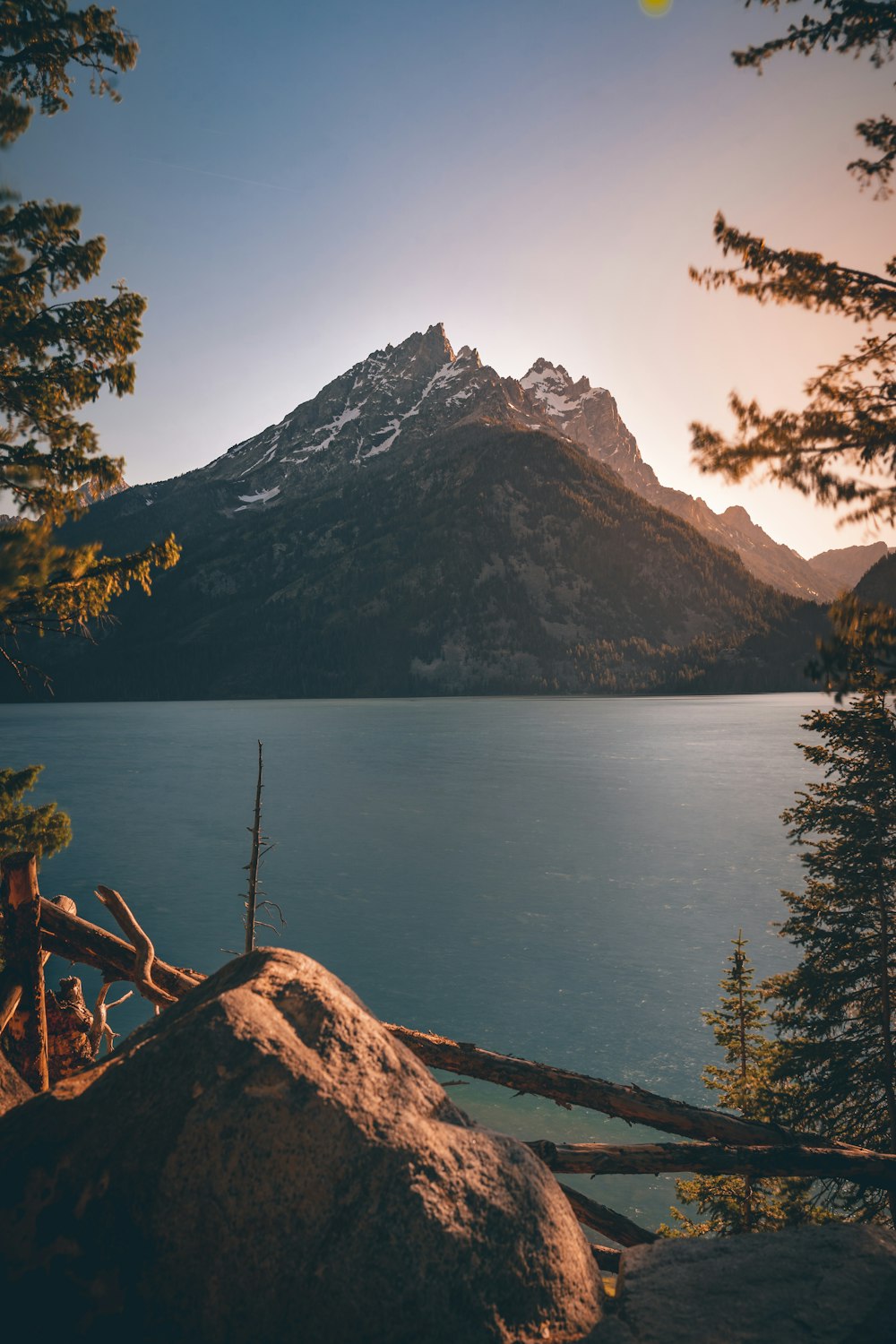 brown wooden bench near body of water and mountain during daytime