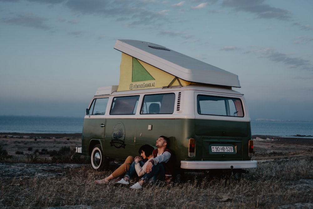 man and woman sitting on ground beside brown van during daytime