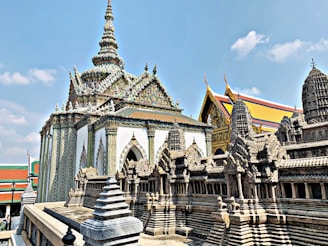 An ornate temple with intricate architectural details and a replica of the Angkor Wat temple. The rooftop features elaborate spires with colorful decorations. The sky is clear and blue, providing a vibrant backdrop.