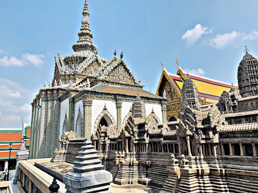 An ornate temple with intricate architectural details and a replica of the Angkor Wat temple. The rooftop features elaborate spires with colorful decorations. The sky is clear and blue, providing a vibrant backdrop.